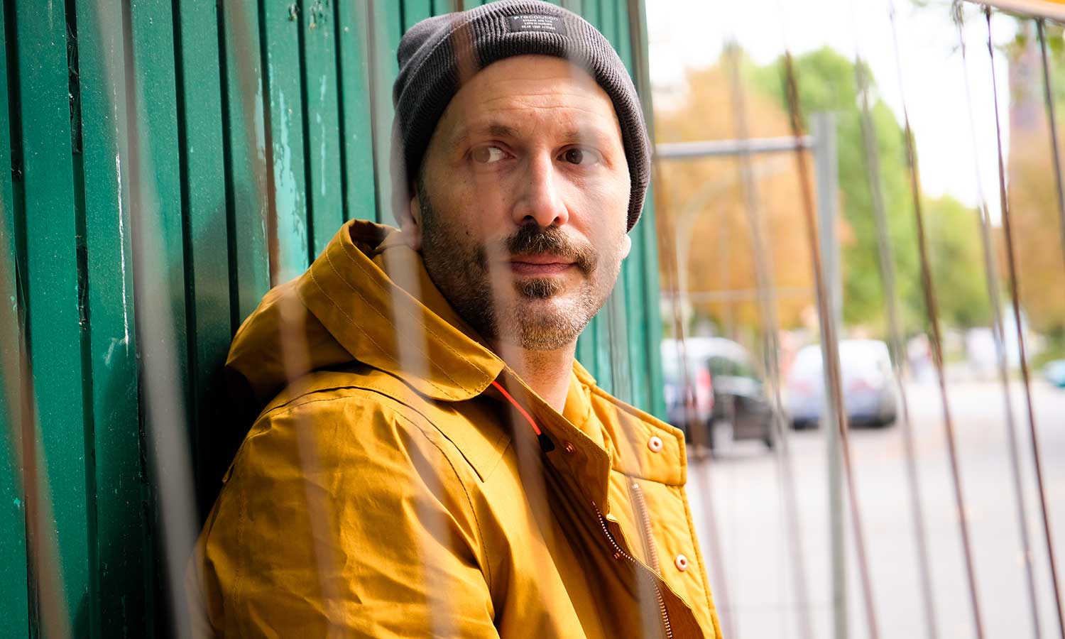 Mann mit gelbem Parka steht vor grünem Bauwagen