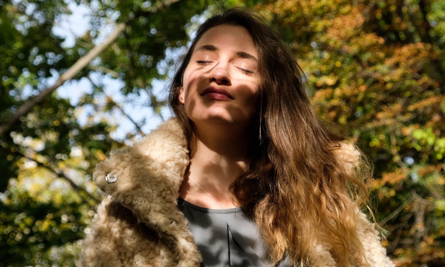Frau steht vor Bäumen und trägt flauschige Winterjacke